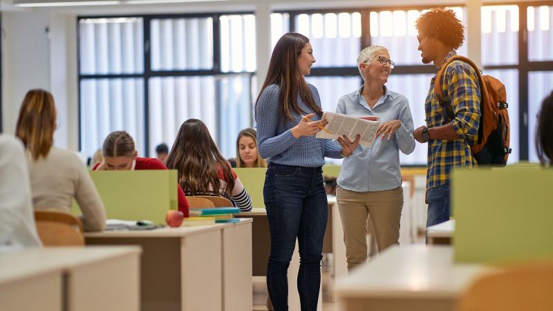 Das Bild zeigt eine Professorin und Studierende im Gespräch.