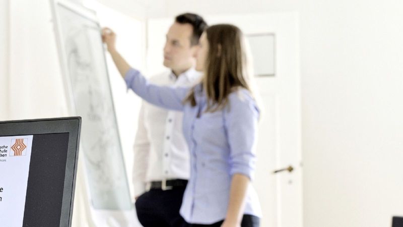 Das Bild zeigt zwei Personen, die auf ein Whiteboard schreiben