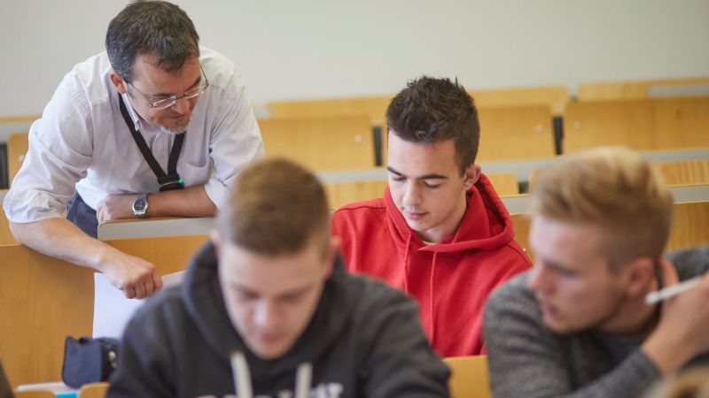 Das Bildt zeigt einen Dozenten und drei Studenten im Hörsaal