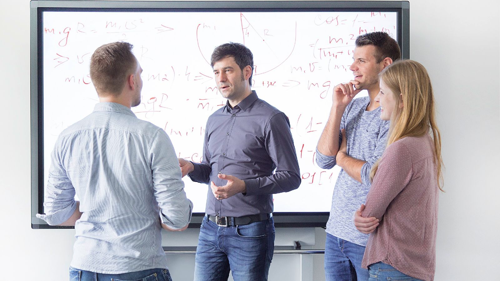 Das Bild zeigt vier Personen, die vor einem Smartboard miteinander sprechen