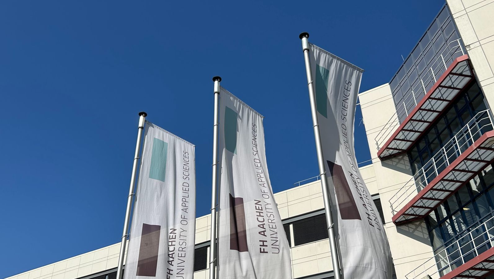 Das Bild zeigt Fahnen vor einem Gebäude der FH Aachen.
